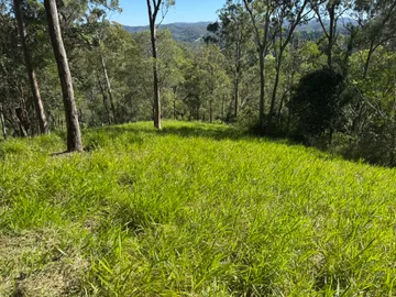 Open grassy acreage slope with distant ranges and blue sky, western Brisbane
